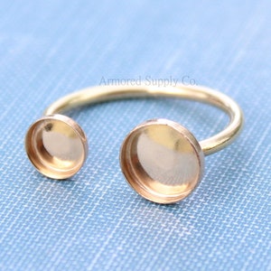 May include: Gold ring with two round, empty, bezel settings. The ring is open and adjustable.