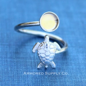 May include: Silver ring with a turtle design and a round bezel setting. The bezel is empty and ready to be filled with resin or a cabochon.