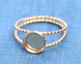 May include: A gold-toned ring with a round, clear glass bezel setting. The ring is made of twisted wire.
