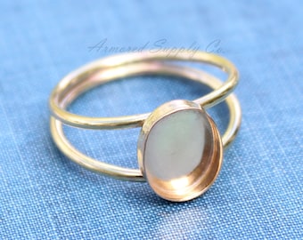 May include: A gold-toned ring with a round, open bezel setting. The ring is made of two bands of metal.