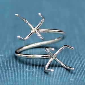 Könnte beinhalten: Silberring mit zwei offenen Fassungen für Steine. Der Ring ist verdreht und hat ein modernes Design.