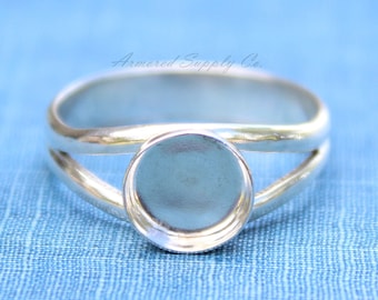 Könnte beinhalten: Ein silberner Ring mit einer runden Zargenfassung. Der Ring ist mit einem geteilten Band gestaltet, was ihm einen einzigartigen und modernen Look verleiht.