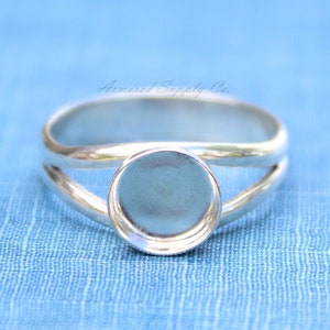 May include: A silver ring with a round bezel setting. The ring is designed with a split band, creating a unique and modern look.