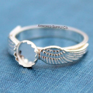 May include: Silver ring with a round bezel and wing design.  The ring is blank and ready to be filled with a stone or other embellishment.  ARMORED SUPPLY CO.