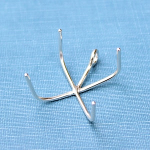 May include: A silver-toned metal pendant with five prongs, resembling a starburst or a small, decorative claw.
