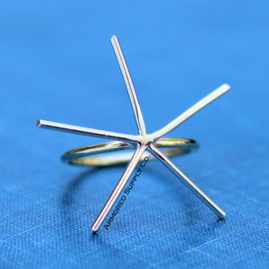 May include: A six-prong ring setting made of silver metal. The setting is designed to hold a gemstone in the center. The setting is on a gold band.