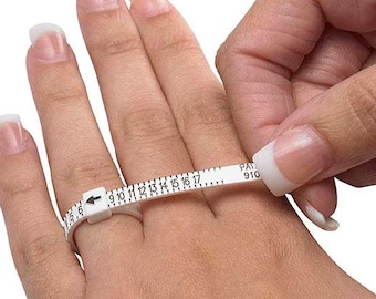 Könnte beinhalten: Ein weißer Kunststoff-Ringgrößenmesser mit schwarzen Markierungen zur Messung von Ringgrößen von 9 bis 17. Der Größenmesser wird verwendet, um einen Finger zu messen.