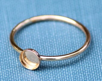 May include: A gold ring with a round bezel setting. The ring is on a blue fabric background.