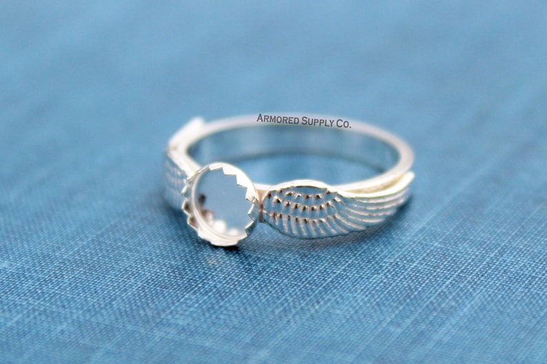 May include: Silver ring with a round bezel and wing design.  The ring is blank and ready to be filled with a stone or other embellishment.  ARMORED SUPPLY CO.