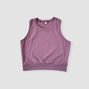 May include: A sleeveless, cropped tank top in a mauve color. The tank top has a round neckline and a relaxed fit.