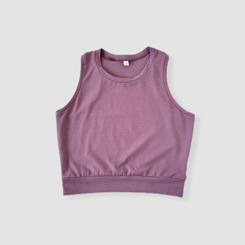 May include: A sleeveless, cropped tank top in a mauve color. The tank top has a round neckline and a relaxed fit.
