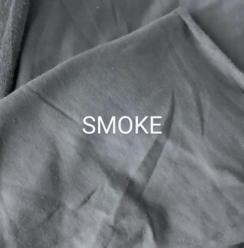 Pu&ograve; includere: Primo piano di un tessuto grigio con la parola "SMOKE" stampata in bianco.