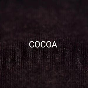 Pu&ograve; includere: Primo piano di un tessuto marrone scuro con la parola "COCOA" stampata in bianco.
