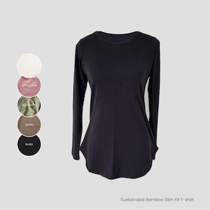 Può includere: Una maglietta nera a maniche lunghe, slim fit, realizzata in bambù sostenibile. La maglietta ha un collo rotondo e un orlo leggermente arrotondato. L'immagine mostra cinque campioni di colore: bianco, rosa vintage, oliva polveroso, terra e nero.