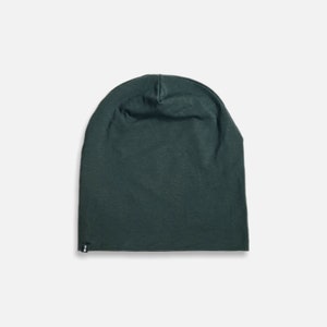 Può includere: Un berretto di colore verde scuro, realizzato in tessuto morbido ed elastico. Il berretto è semplice e non ha decorazioni.