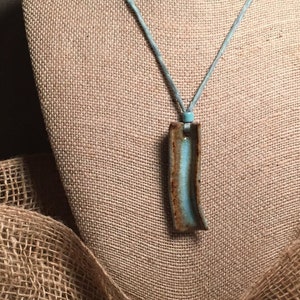 May include: A turquoise and brown ceramic pendant necklace on a brown suede cord. The pendant is a rectangular shape with a curved edge.