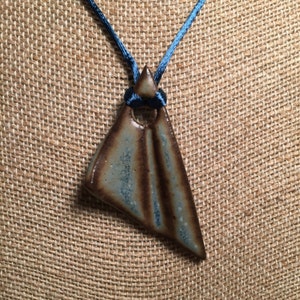 May include: A blue and brown ceramic triangle pendant with a hole in the center, hanging from a blue ribbon.