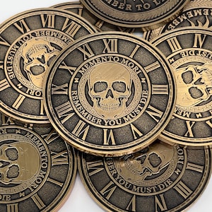 May include: A stack of gold-colored metal coins with a skull and clock face design. The coins feature the text "Memento Mori" and "Remember You Must Die".