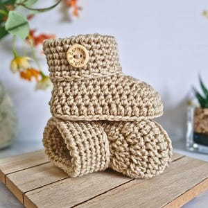 Handmade crochet baby booties with a neat folded cuff, finished with Born in 2026 wooden buttons, sizes newborn, 0-3 and 3-6 months and multiple colour choices - cute baby shower gift