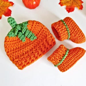 May include: A handmade orange crochet pumpkin hat with green stem and leaf details, and matching orange booties with green trim. Ideal for a baby's first Halloween or autumn-themed photoshoot. The set is made of soft yarn.