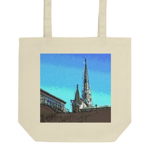 Może przedstawiać: Torba typu tote z grafiką wieży kościelnej na tle niebieskiego nieba. Kościół jest brązowy, a niebo jasnoniebieskie z odcieniem zieleni.