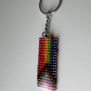 May include: A rainbow beaded keychain with a silver key ring and chain. The beads are arranged in a rainbow pattern with a white cloud at the bottom.