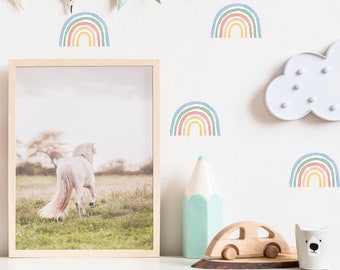 May include: A white wall with a garland of colorful flags hanging across the top. There are several rainbow decals on the wall, along with a white cloud-shaped light. A white stuffed animal head, a wooden toy car, a light blue pencil, and a white mug with a bear face are on a white shelf.