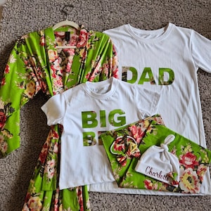 May include: A family pyjama set with a green floral design. The set includes a robe, two white t-shirts with "DAD" and "BIG BRO" in green, and a pair of trousers. A matching headband and a white hat with the name "Charlotte" are also included.