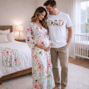 May include: A person wearing a light blue floral print robe with pink flowers, standing with a person wearing a white t-shirt with the word "DAD" in a floral design. A matching floral blanket is on the bed.
