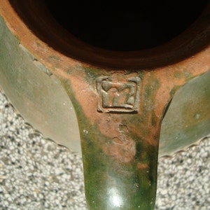 Peut inclure: Une cruche en c&eacute;ramique &eacute;maill&eacute;e verte avec un bord brun et une marque estampill&eacute;e au fond. La cruche a une anse et un bord festonn&eacute;.