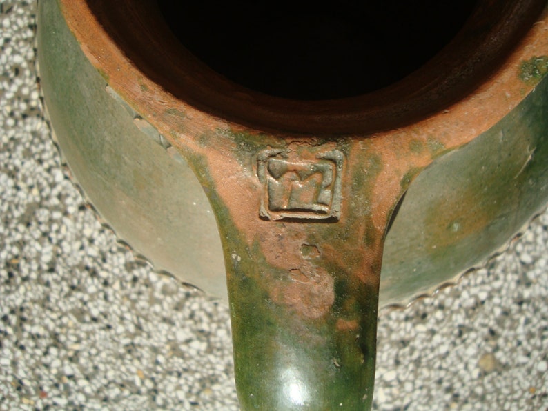 Peut inclure: Une cruche en c&eacute;ramique &eacute;maill&eacute;e verte avec un bord brun et une marque estampill&eacute;e au fond. La cruche a une anse et un bord festonn&eacute;.