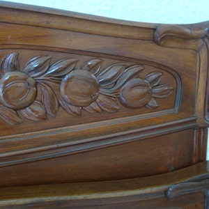 May include: A dark wood headboard with intricate carvings of leaves and fruit. The headboard is curved at the top and has a decorative design on the side.
