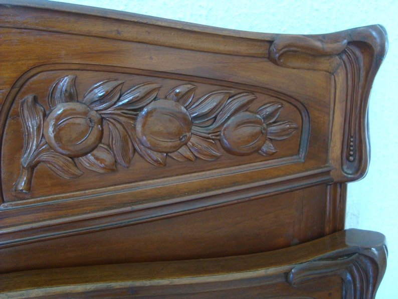 May include: A dark wood headboard with intricate carvings of leaves and fruit. The headboard is curved at the top and has a decorative design on the side.