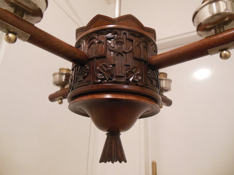 May include: A wooden chandelier with a carved design and five light fixtures. The chandelier has a dark brown finish and a decorative, pointed bottom.