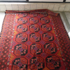 May include: A red, black, and blue patterned rug with a geometric design. The rug has a fringe border.