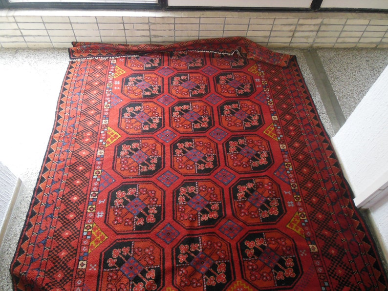 May include: A red, black, and blue patterned rug with a geometric design. The rug has a fringe border.