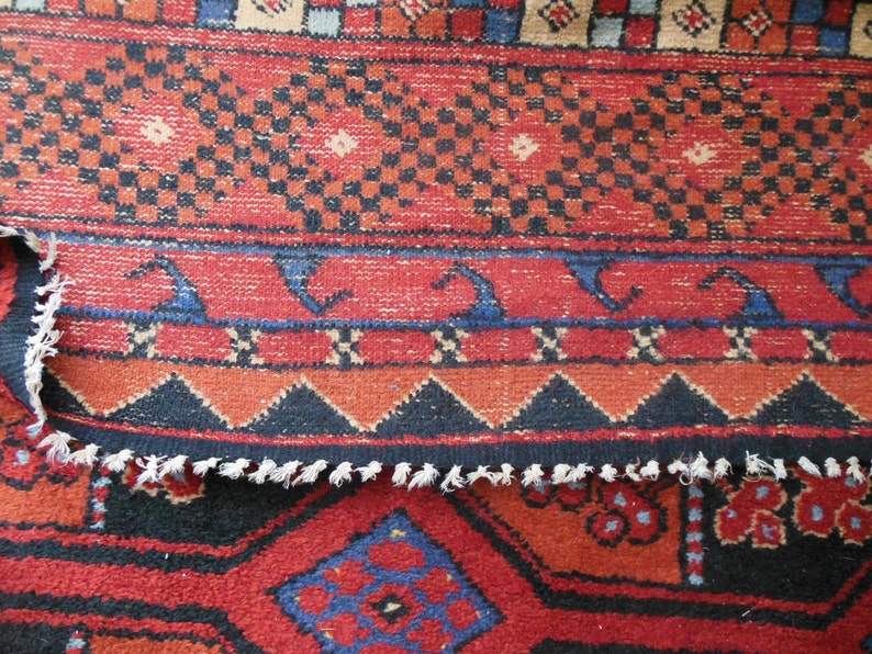 May include: Close-up of a red, blue, and black patterned rug with a fringed edge. The rug has a geometric design with repeating patterns.