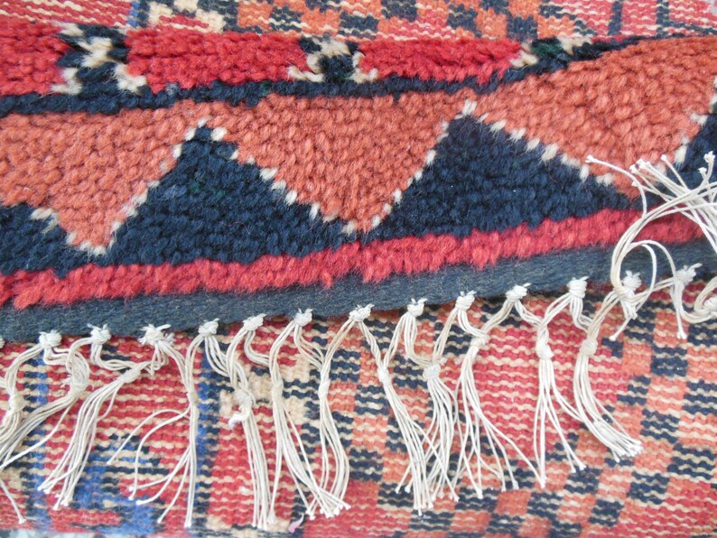May include: Close-up of a red, black, and white woven rug with fringe. The rug has a geometric pattern with triangles and squares.