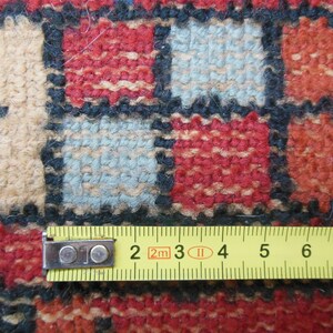 May include: Close-up of a colorful woven rug with a measuring tape placed across the bottom edge. The tape reads "2m 3 4 5 6 7 8".