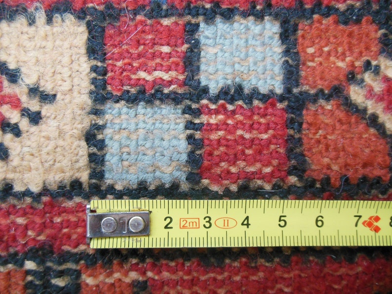 May include: Close-up of a colorful woven rug with a measuring tape placed across the bottom edge. The tape reads "2m 3 4 5 6 7 8".