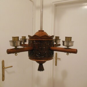 May include: A wooden chandelier with five candle holders. The chandelier is carved with intricate details and has a dark brown finish.