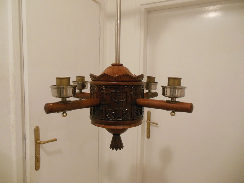 May include: A wooden chandelier with five candle holders. The chandelier is carved with intricate details and has a dark brown finish.