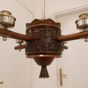 May include: A wooden chandelier with four lights, each with a silver and brass cup-shaped shade. The chandelier has a carved wooden base with intricate details.
