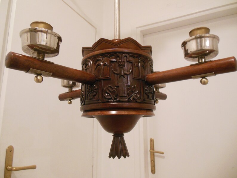 May include: A wooden chandelier with four lights, each with a silver and brass cup-shaped shade. The chandelier has a carved wooden base with intricate details.