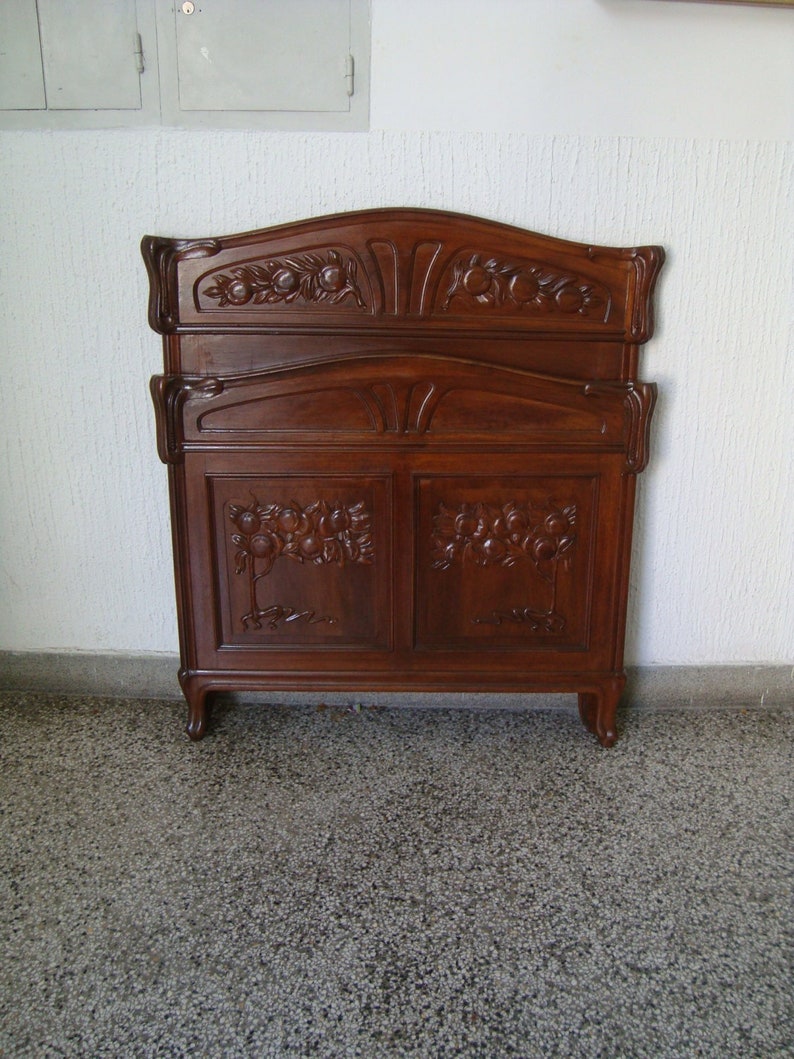 May include: A dark wood headboard with intricate carvings of fruit and leaves. The headboard is in the Art Nouveau style.