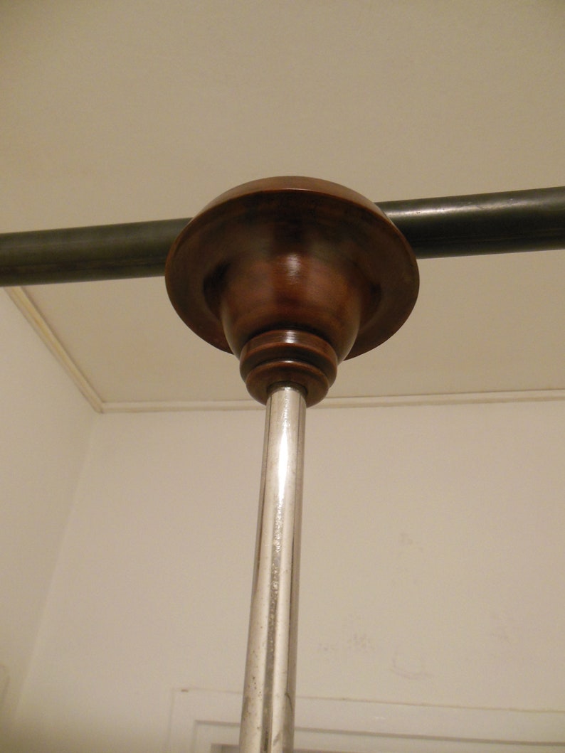 May include: A close-up of a ceiling mounted light fixture with a brown wooden canopy and a silver metal pole.