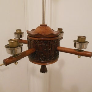 May include: A wooden chandelier with four candle holders. The chandelier is carved with intricate designs and has a dark brown finish.