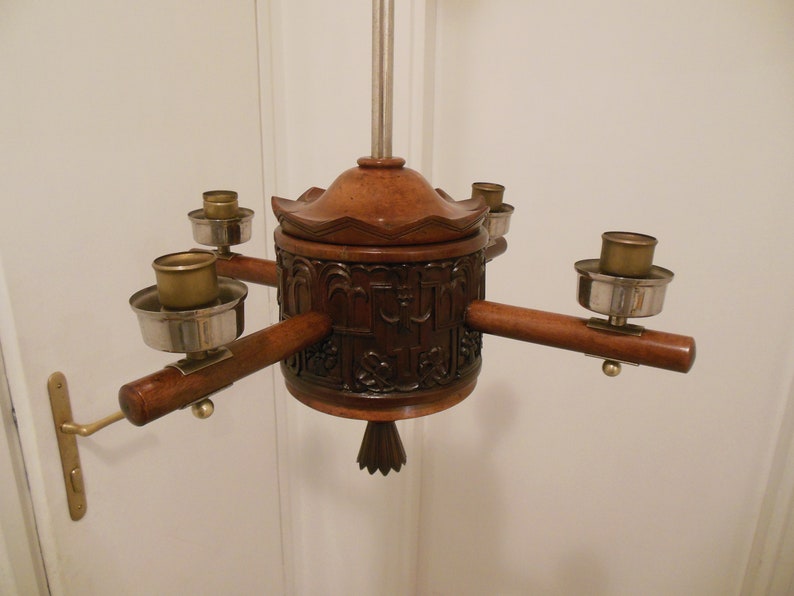May include: A wooden chandelier with four candle holders. The chandelier is carved with intricate designs and has a dark brown finish.
