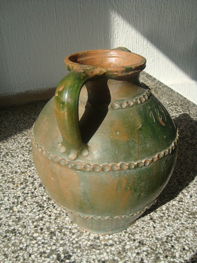 Peut inclure: Une cruche en c&eacute;ramique verte et brune avec une anse et un motif de perles. La cruche porte le num&eacute;ro 1891 sur le c&ocirc;t&eacute;.