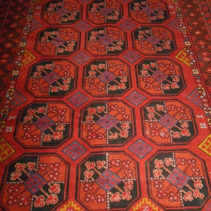 May include: A red rug with a geometric pattern of black, red, and blue. The rug has a border of black, white, and yellow.